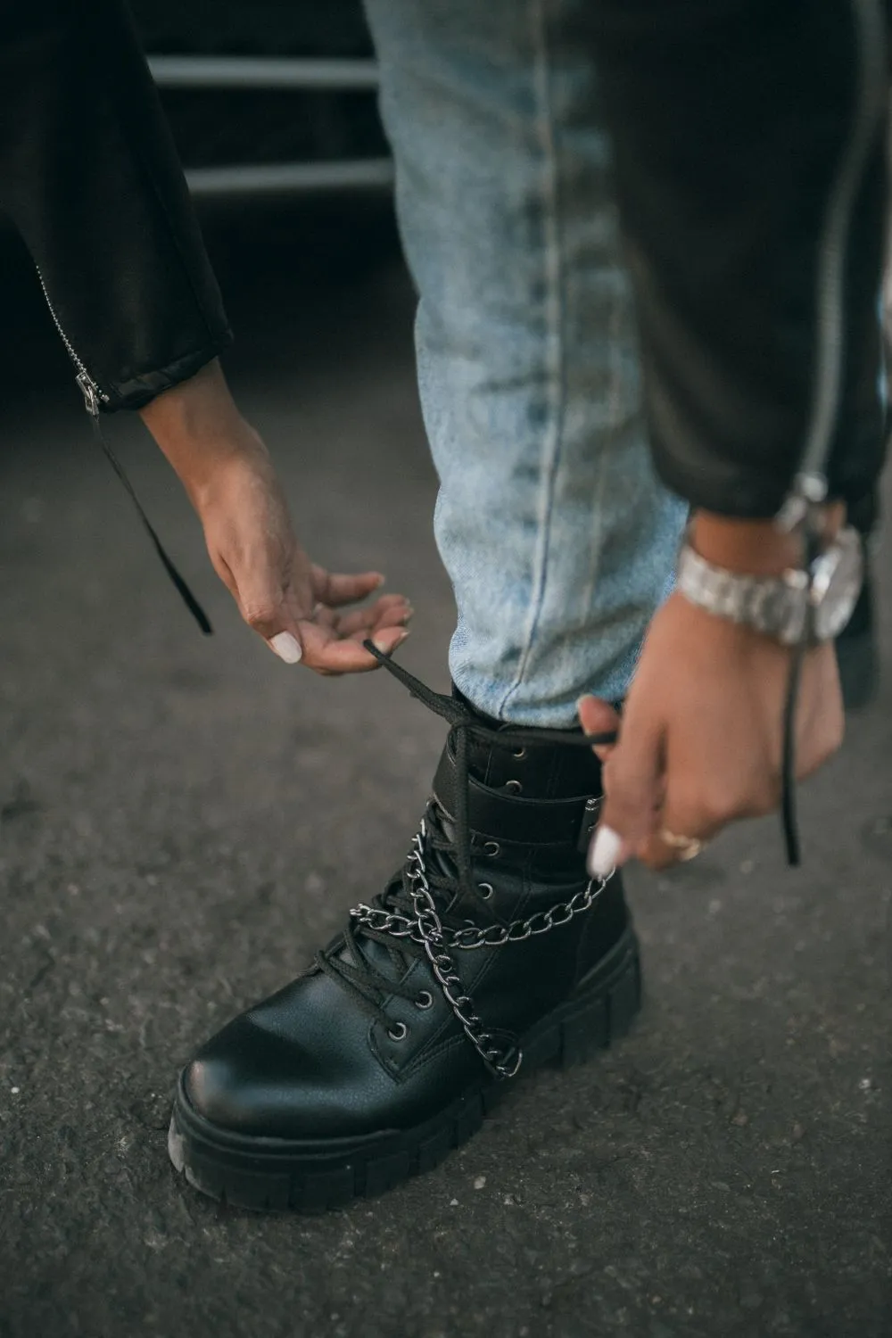 Persona amarrándose los cordones de un botín negro en la calle