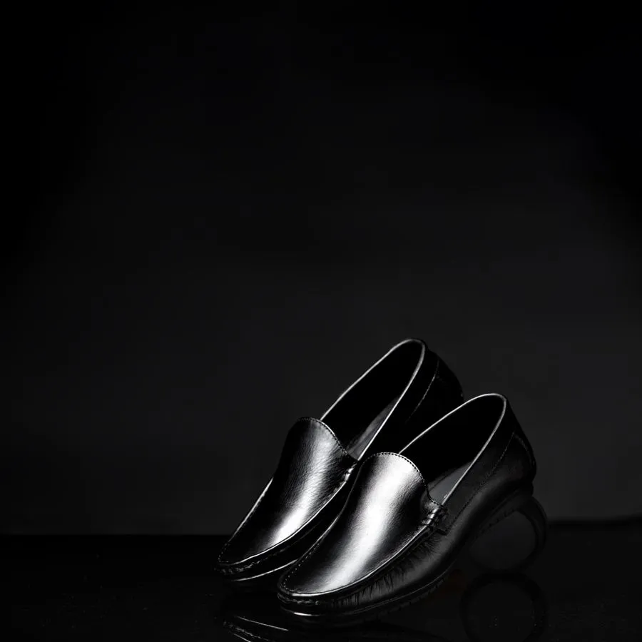 Par de mocasines de cuero negro sobre una superficie oscura y brillante