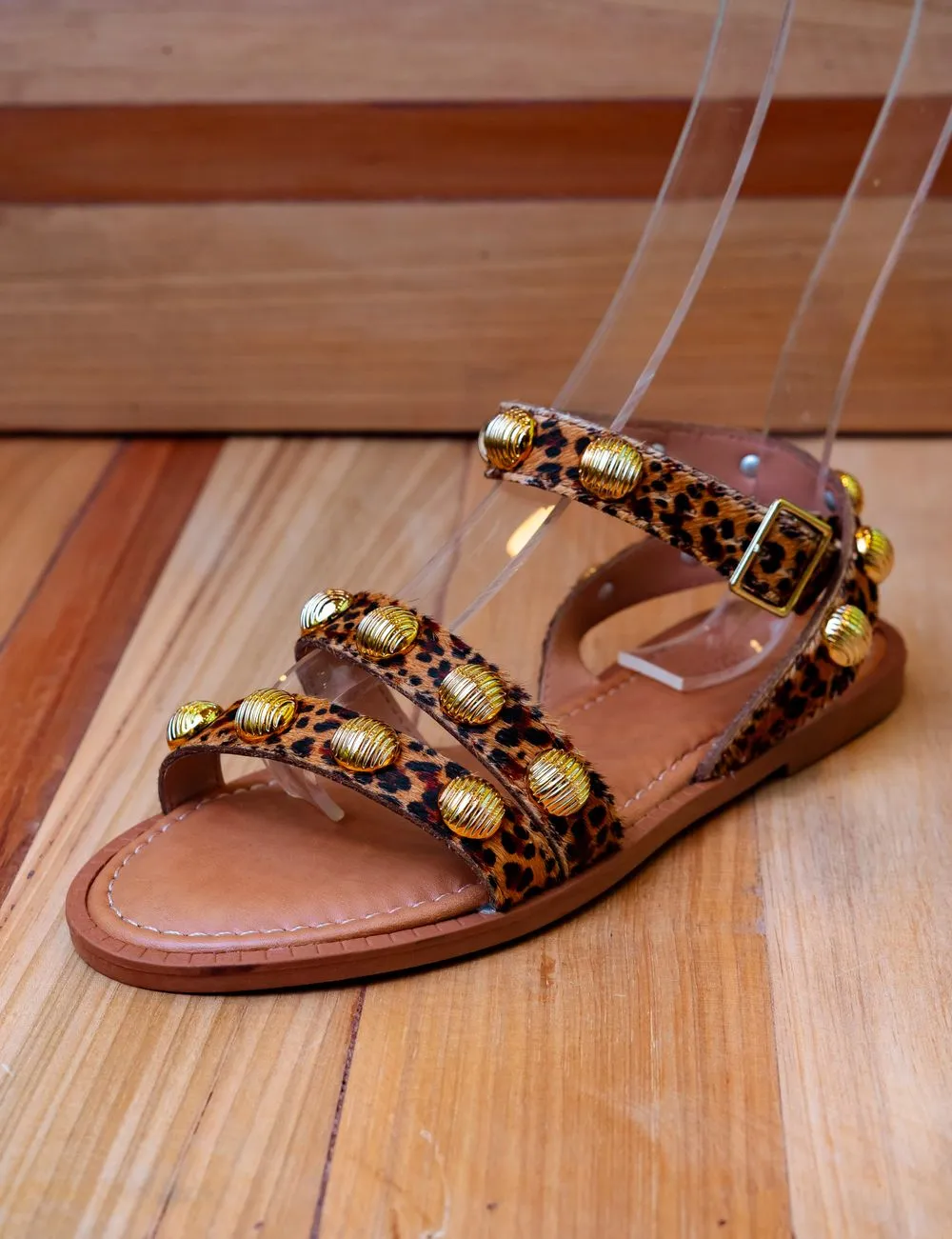 Sandalia de tiras con estampado animal y apliques dorados sobre piso de madera