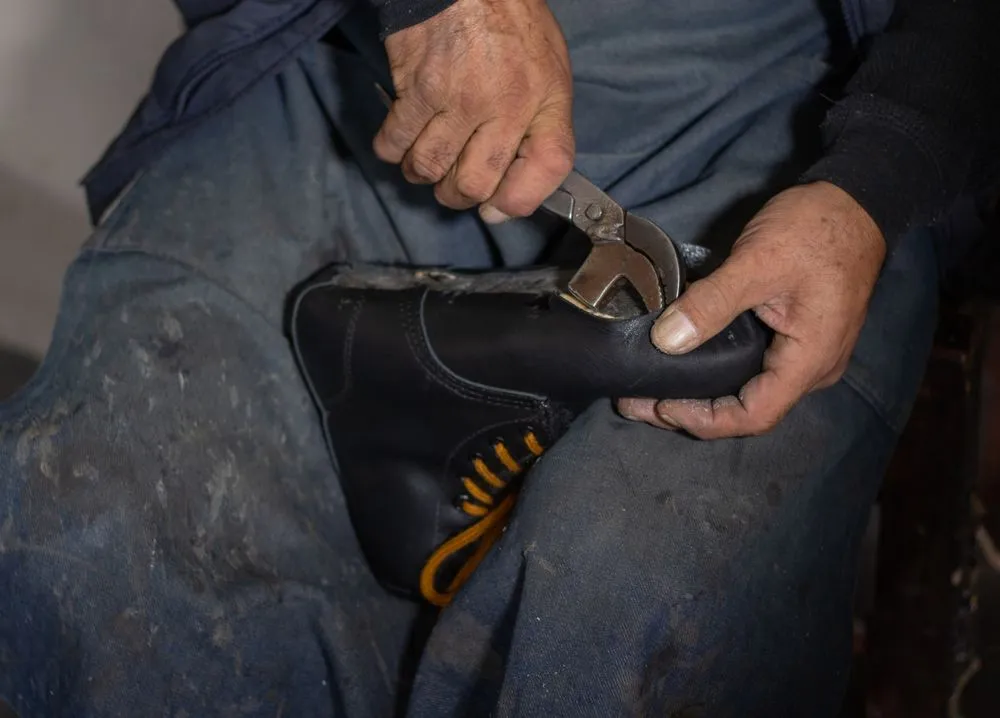 Zapatero sujetando un botín negro mientras le retira la suela con una pinza