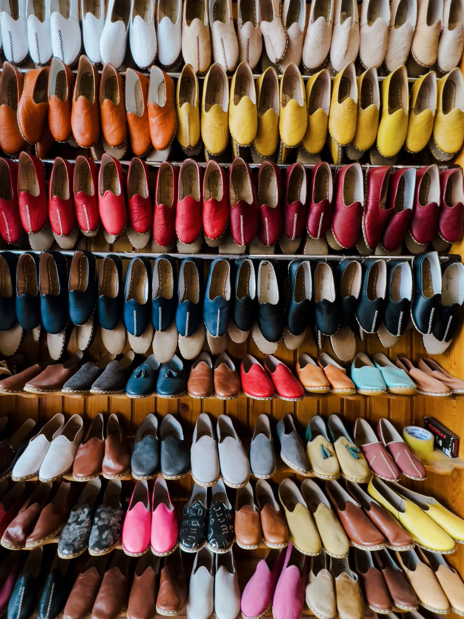 Pared de una zapatería cubierta de estantes con zapatos de colores ordenados por fila